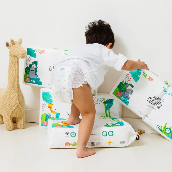 A baby playing with packs of Les Petits Culottés nappies